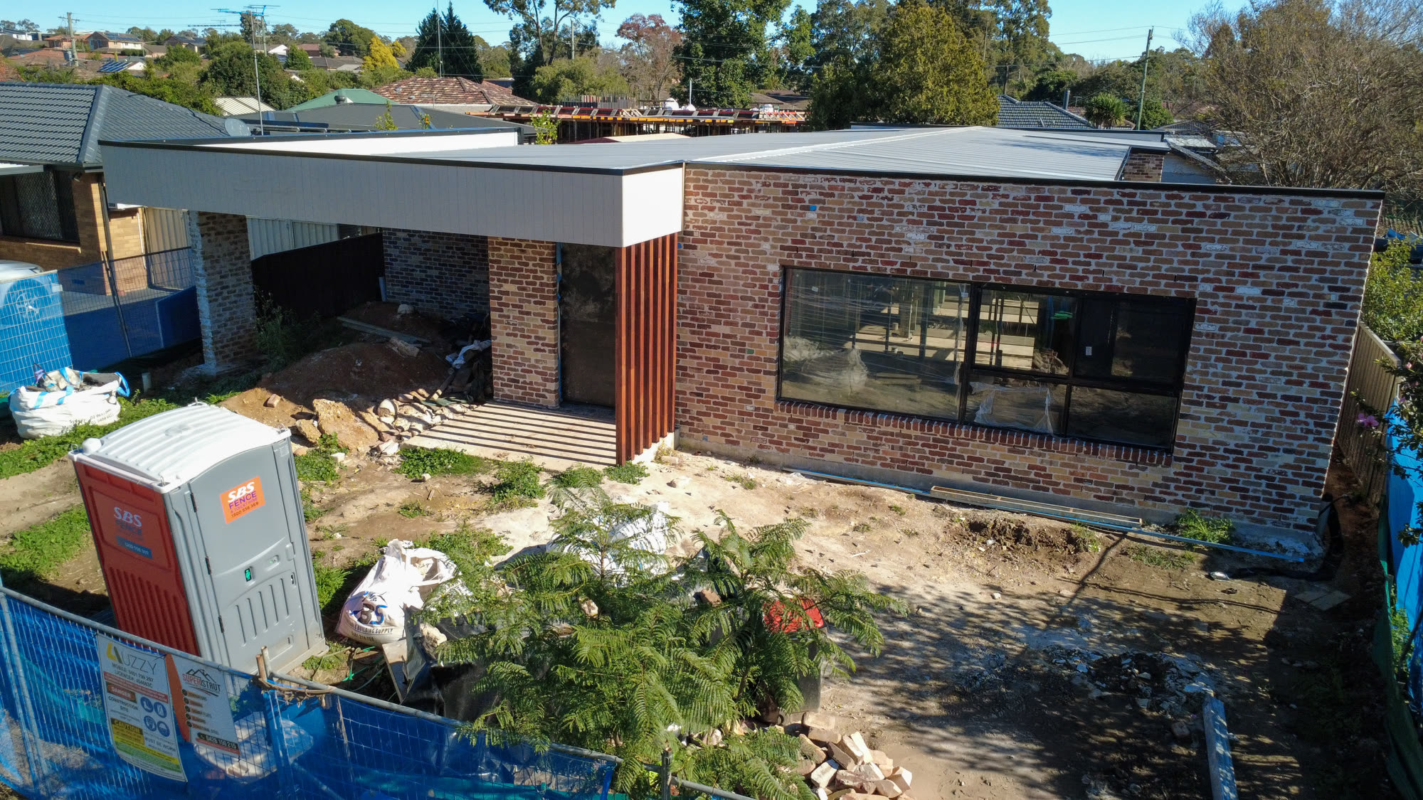 Aerial view of an Auzzy Projects build in progress in Western Sydney, with site fencing around the block, brickwork and cladding underway and materials stacked on the ground